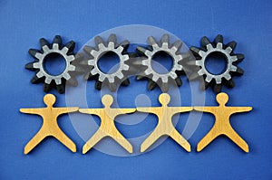 Metal cogs cogwheels and wooden figures of people holding hands