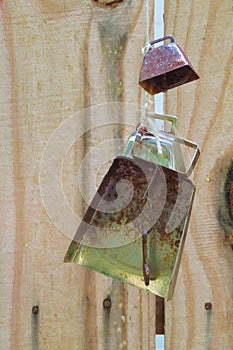 Metal cowbells hanging on string from wood fence