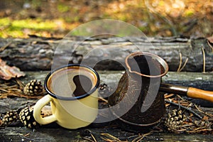Metal cup with hot coffee and cezve on the wooden background with the coins, needles and bark of tree.