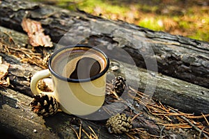 Metal cup with hot coffee on the wooden background with the coins, needles and bark of tree.