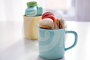 Metal cup with tasty colorful macarons on white table