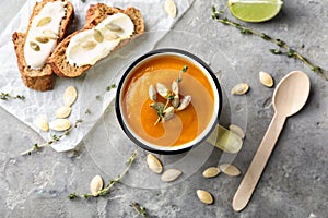 Metal cup with tasty pumpkin cream soup on grey table