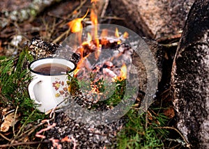 Metal cup with tea heats by the fire, autumn time, burning firewood, branches and smoke, autumn