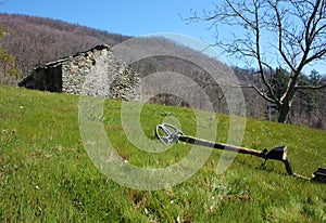 A metal detector resting on a lawn, lying on a very green clearing, a field of the Apuan Alps in Tuscany. in front of an abandoned