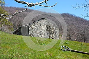 A metal detector resting on a lawn, lying on a very green clearing, a field of the Apuan Alps in Tuscany. in front of an abandoned