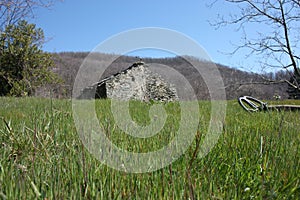 A metal detector resting on a lawn, lying on a very green clearing, a field of the Apuan Alps in Tuscany. in front of an abandoned