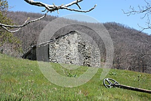 A metal detector resting on a lawn, lying on a very green clearing, a field of the Apuan Alps in Tuscany. in front of an abandoned