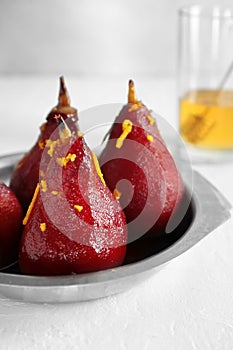 Metal dish with delicious poached pears in red wine on white table