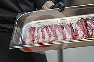 Metal dish in hand of cook with sliced pieces of meat