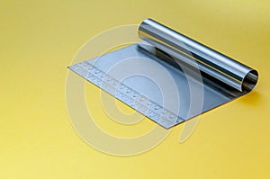 Metal dough scraper knife over bright yellow surface background. Stainless steel flat dough scraper with Ruler scale.