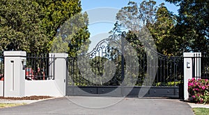 Metal driveway entrance gates set in brick fence with garden trees in background