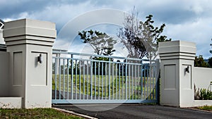 Metal driveway private residence property entrance gates set in brick fence with garden trees in background