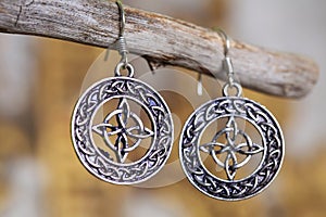 Metal earrings in ornamental shape hanging on neutral background