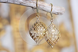 Metal earrings in ornamental shape hanging on neutral background