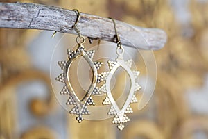 Metal earrings in ornamental shape hanging on neutral background