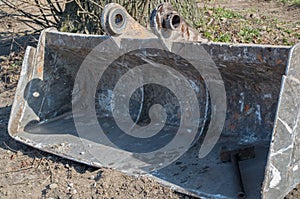 Metal excavator bucket with stiffening ribs inside and eyelets on top, at the bottom of bucket on right is sledgehammer.