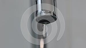 Metal faucet nozzle dripping water droplets close up macro shot.