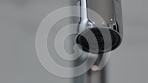 Metal faucet nozzle dripping water droplets close up macro shot.