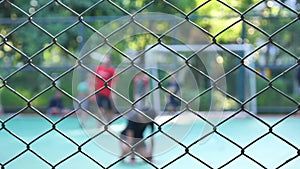 Metal fence against blurred background, close up. Unrecognized people playing football with fence in front. 4k