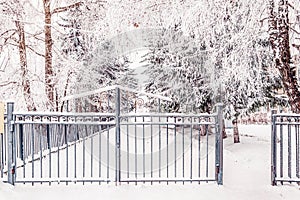 Metal fence with entrance gate along the snow-covered path. Winter Snow urban landscape