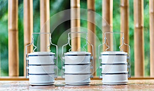 Metal food carriers on a wooden table, a bamboo backdrop.