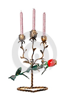A metal forged candlestick in the form of rosebuds with three candles stands on a twisted stand with a red forged rose isolated on