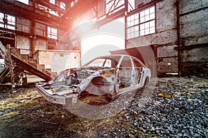 Metal frame of a rusty car in a big old abandoned building inside with light leaks