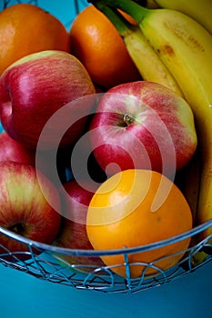 Metal fruit bowl on a wooden surface. Close. Bananas, oranges and apples