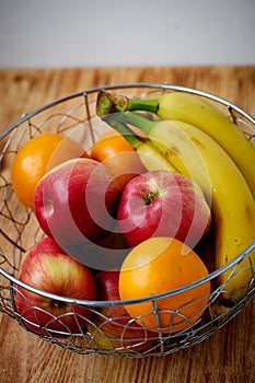 Metal fruit bowl on a wooden surface. Close. Bananas, oranges and apples