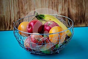 Metal fruit bowl on a wooden surface. Close. Bananas, oranges and apples