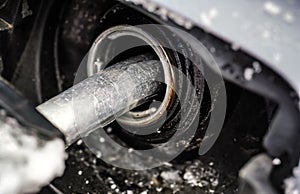 Metal fuel nozzle, filling gas tank of car covered with snow in winter, closeup detail