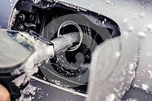 Metal fuel nozzle, filling gas tank of car covered with snow in winter, closeup detail.