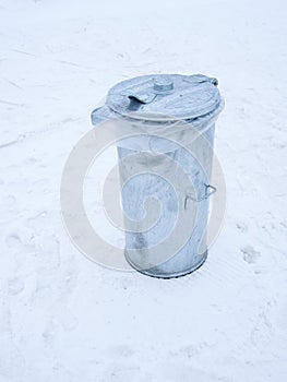 Metal garbage can with lid closed on the snow