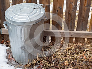 A metal garbage can sits by the fence ready for spring cleaning.