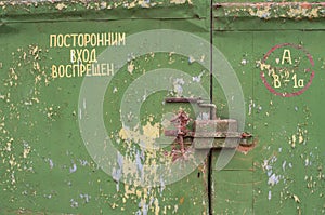 The metal gate is padlocked. Rusty padlock on the gate, close-up. Rough iron doors painted green