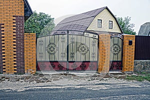 Metal gates with a forged pattern on the street and part of the brick fence