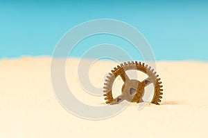 A metal gear, brass in the sand, a gear sticking out of the sand