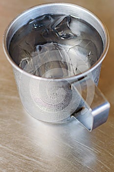 Metal glass or cup of cold water with ice on stainless steel tab