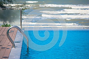 Metal grab bar ladder in blue water swimming pool with sea wave background.