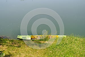 Metal, green colored boat in river water, moored to the shore, river bank, with green grass coast