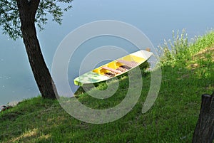 Metal, green colored boat in river water, moored to the shore, river bank, with green grass coast