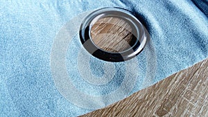 Metal grommet on a gray-blue velvet curtain. The fabric lies on a wooden table. The hole on the material is made of silver coated photo