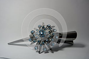 Metal hair clip for women with a large metallic flower and decorated with small blue stones and located on a white background.