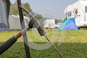 Metal hammer putting a nail-like tent peg out of iron into the grass.