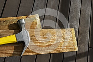 A metal hammer with a yellow and black wooden handle on wooden planks in a room with dark wooden floors