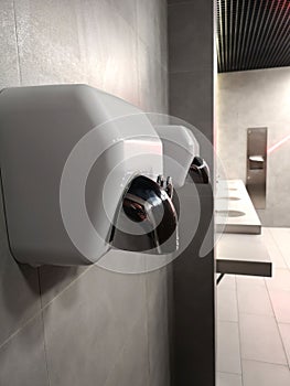 Metal hand dryer on the white tiled wall