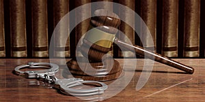 Metal handcuffs and judge gavel on wooden desk, law books background. 3d illustration