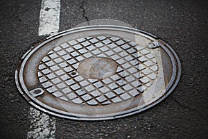 Metal hatchway. Old, cracked, round hatchway with minimalistic ornament on a road background. Old pavement in the city.