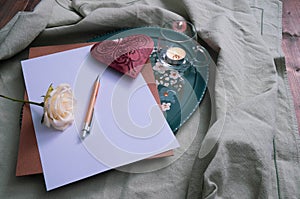 Metal heart and white rose, writing materials on the table, near a candle and decorations