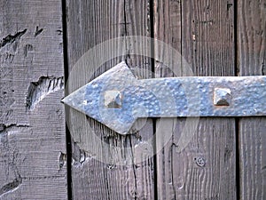 Metal hinge with a shape of an arrow pointing left over an old door
